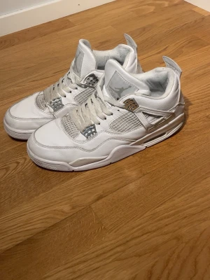Nike Air Jordan 4 Pure moneys - Säljer ett par Nike Air Jordan 4 Retro i helvitt med kromade detaljer. Skorna har snörning, meshpaneler och den ikoniska Jumpman-loggan på hälen. Tillverkade i skinn med platt sula och rund tå. Perfekta för dig som vill ha en clean och klassisk sneaker.