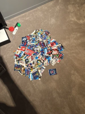 Ingen väst synlig på bilden - Bilden visar ingen väst, utan ett stort antal samlarkort utspridda på ett golv. Ingen väst kan beskrivas eller taxonomier matchas.