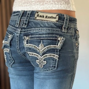 Rock revival jeans - Lågmidjade bootcut jeans från rock revival. Snygg design. Mycket bra skick, se bild. Mått: Innerbenslängd: 84cm   Midjemått rakt över: 35cm. Utsydda där nere då dom var lite korta så skulle säga att det är kanske 86-87 i innerbenslängd