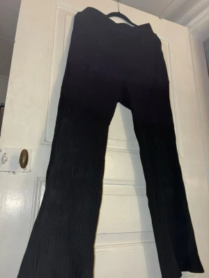 Svarta ribbade byxor i stickat material kay/day - Svarta ribbade byxor i stickat material med bred resår i midjan från kay/day. Byxorna har en rak och lite utsvängd passform, vilket ger en chill och trendig vibe. Perfekta att styla med en oversized hoodie eller ett linne för en avslappnad look. Kommer även att sälja ett tillhörande linne separat.