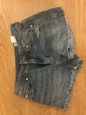Blå jeansshorts ARIEL mid waist - Säljer ett par blå jeansshorts från ARIEL i storlek 152. De har midwaist-passform, råa fransiga kanter och slitna detaljer både fram och bak. Klassisk femficksmodell i bomull, perfekta för sommardagar.