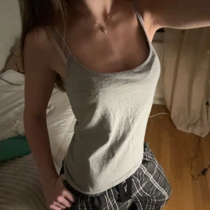 Grå enkel linnetopp - Säljer en basic grå linnetopp med smala axelband och rak halsringning. Toppen är i mjuk bomull och har en klassisk, stilren look som passar till allt. Perfekt att matcha med jeans eller shorts för en chill vibe.