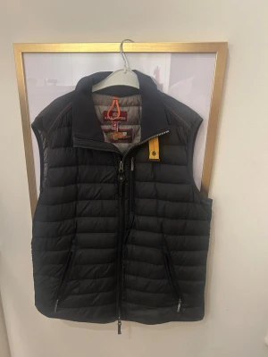 Svart dunväst från Parajumpers  - Säljer en svart dunväst från Parajumpers i superlätt modell. Västen har ståkrage, två dragkedjefickor och en gul detalj vid halsen. Klassisk quiltad design och stängs med dragkedja framtill. Perfekt för lager-på-lager under kyliga dagar. Knappt använd den och mer bilder kan diskuteras!