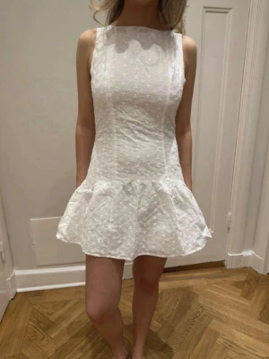 Vit kort klänning med öppen rygg - Supersöt vit kortklänning med broderade blommor. Klänningen har en volangkant nedtill, är ärmlös och har en snygg öppen rygg med knytband i nacken. Helt ny med lappar kvar ifrån peppermayo, de har lite konstiga storlekar men passar 36-38. Helt perfekt till studenten.