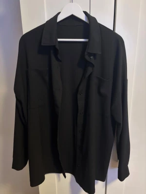 Svart oversized skjorta med knappar - Säljer en svart oversized skjorta med klassisk krage och knäppning framtill. Skjortan har långa ärmar och två stora fickor. Står storlek XS men är mer som L/XL 🩷