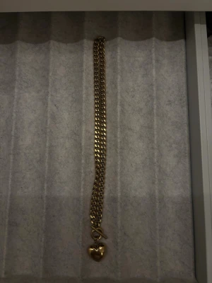 Guldigt armband med hjärthänge EDBLAD, kedja  - Säljer ett chunky armband från EDBLAD i guldtonad metall med ett gulligt hjärthänge. Länken är bred och armbandet har en snygg toggle-låsning. Perfekt accessoar för att lyfta vilken outfit som helst.