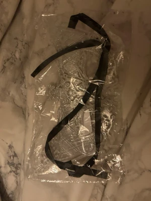 Glittrig silver mask med svarta band - Säljer en snygg maskeradmask i silver med glittrig yta och detaljerat mönster. Masken har svarta band för att knyta runt huvudet och passar perfekt till maskerad eller temafest. Materialet är lätt och bekvämt att bära.