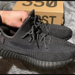Adidas Yeezy Boost 350 V2 Black - Säljer ett par Adidas Yeezy Boost 350 V2 i helsvart. Skorna har stickad ovandel i svart mesh, rund tå, snörning och en chunky, räfflad sula i svart gummi. Diskret röd söm på hälen och klassisk Yeezy-design. Perfekta för dig som vill ha en clean och modern sneaker.