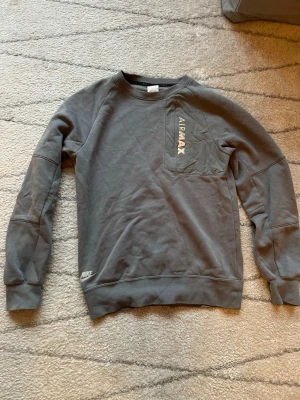 Grå Nike Air Max sweatshirt - Säljer en grå Nike Air Max sweatshirt med tryck på bröstet och en cool fickdetalj. Tröjan har rund hals, långa ärmar och är tillverkad i mjuk bomullsmix. Perfekt för dig som gillar streetwear och sportig stil. Använd fåtalet gånger där av inga defekter 