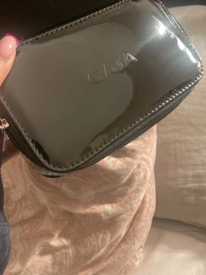 Svart necessär från CAIA i syntet - Säljer en stilren svart necessär från CAIA med glansig finish och dragkedja runtom. Perfekt storlek för smink eller småprylar, med ett fack på insidan. Materialet är syntet och ytan är riktigt blank och snygg OBS helt ny, säljer pga att jag har två st.