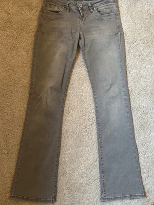 Grå bootcut jeans från LTB, 25/30 - Säljer ett par grå jeans från LTB i bootcut-modell med låg midja. Jeansen har klassisk femficksdesign, knapp och dragkedja fram samt snygga detaljer på bakfickorna. Materialet är mjukt denim i bomull och passar dig som gillar en avslappnad stil. Ordinarie pris är 799, säljer för 500. I mycket bra skick, bara använt få gånger.