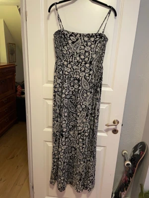 Svartvit långklänning med mönster - Långklänning med smala axelband i svart och vitt. Klänningen har ett detaljerat paisleyinspirerat mönster🥰. Luftigt tyg som passar perfekt till varma dagar!! Jag är 175cm och den går ner till fötterna på mig, så den är rätt lång😊💕