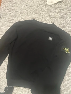  Stone Island tröja - Svart sweatshirt från Stone Island med klassisk patch på ärmen och broderad logga på bröstet. Tröjan har rund halsringning och långa ärmar. Tillverkad i mjuk bomull för skön känsla och stilren look.
