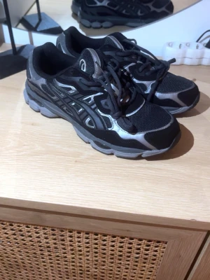 Asics sneakers - Säljer ett par snygga Asics sneakers i svart och silver. Skorna har meshpaneler för bra ventilation, detaljer i syntet och klassisk snörning. Sulan är rejäl och ger bra stöd, perfekt för dig som gillar sportig stil. Loggan syns tydligt på sidan och plösen.