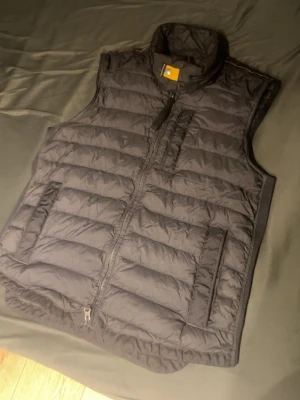 Svart parajumpers väst - Säljer en svart dunväst från Parajumpers Remix i storlek S. Västen har quiltad design, hög krage och dragkedja framtill. Flera praktiska fickor och snyggt broderat märke på ryggen. Perfekt för lager-på-lager under kyliga dagar.