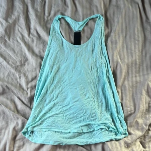 Turkos linnetopp från Drop of Mindfulness - Säljer en turkos linnetopp från Drop of Mindfulness. Toppen har brottarrygg med svart detalj och tryckt logga på ryggen. Tillverkad i mjuk viskos, perfekt för träning eller chill dagar. Enkel och snygg design som är lätt att matcha med tights eller shorts.