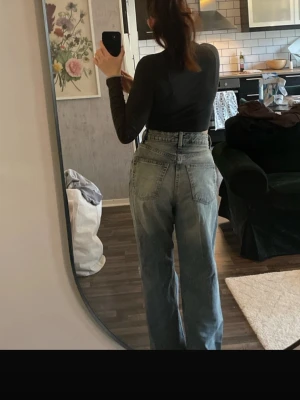 Blåa high waist wide jeans - Säljer ett par blåa jeans med hög midja och breda ben. Jeansen har klassiska fem fickor och en snygg sliten detalj med hål på ena knät. Passformen är loose och de är tillverkade i jeansmaterial. Perfekta för dig som gillar en avslappnad och trendig stil.