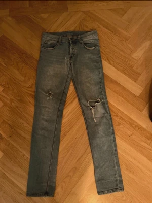 Cheap Monday  skinny jeans med slitningar - Snygga blå Cheap Monday jeans med skinny passform och slitningar på båda benen. Klassisk femficksmodell med orangea sömmar och Cheap Monday-logga på bakfickan. Jeansen har låg midja och är gjorda i jeansmaterial med dragkedja och knapp framtill.