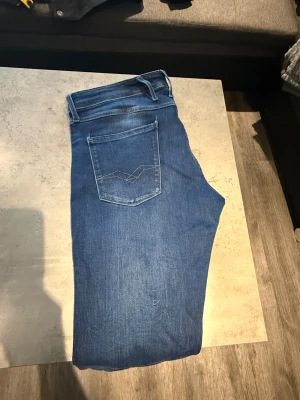 Replay blå jeans  - Säljer ett par snygga blå jeans från Replay med klassisk femficksdesign och raka ben. Jeansen har ljus tvätt, tydliga sömmar på bakfickorna och Replay-märke på linningen.  34/34. Använd 2-3 ggr