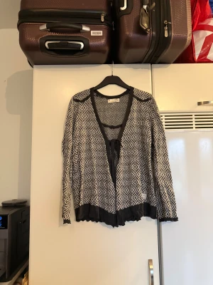 Svartvit kofta Odd Molly med knyt - Säljer en svartvit kofta med grafiskt mönster och snygga mörkgråa detaljer. Koftan har lång ärm, v-ringad öppning och knytband framtill. Nederkanten har en volang som ger extra stilpoäng. Perfekt att slänga på över en topp! Från märket Odd Molly. Storlek 2 som enligt deras storleksguide motsvarar en M. Mycket fint skick, jag hittar inga synliga anmärkningar eller defekter.  