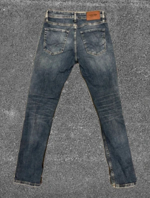 Blå jeans från Jack & Jones - Snygga blå jeans från Jack & Jones med klassisk femficksdesign. Jeansen har en rak passform och är tillverkade i slitstarkt denim med lätt tvättad look och subtila slitningar framtill. Perfekta för dig som gillar en enkel och stilren jeansstil. Modell: SLIM/GLENN. Storlek: W38 & L32