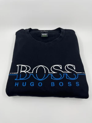Svart Hugo Boss sweatshirt slim fit - Svart tröja från Hugo Boss i slim fit med stor vit och klassisk BOSS- logga på bröstet. Perfekt för dig som gillar stilrena och klassiska designer med en modern touch. Tröjan har använts ett fåtal gånger med varsamhet men är nästan helt ny. Hör av er vid frågor!😇 Pris kan diskuteras! Skriv om mer bilder!