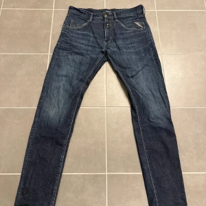 Replay jeans blå tapered 33/34 - Snygga blå jeans från Replay med klassisk femficksdesign och guldfärgade detaljer vid knappen. Jeansen har en tapered passform och är tillverkade i slitstarkt denimtyg. Perfekt för dig som gillar stilrena och tidlösa jeans med cool tvätt.