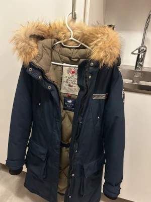 Lexington Ranger Down Parka – mörkblå, stl XS (pris diskuterbart) - Säljer en mörkblå Lexington The Lexington Ranger Down Parka i storlek XS. Jackan är i mycket gott skick och har använts under cirka tre vintrar. Inga fläckar, revor eller skador och innerfodret är rent och fräscht. Pälsen är avtagbar och i jättebra skick. Jackan är varm med dunfyllning (650 fill power) och har dragsko i midjan så den går att dra åt för en figurnära passform. En klassisk och tidlös vinterjacka av hög kvalitet.  Pris: 1499 kr, men priset kan diskuteras vid snabb affär. Kan hämtas 