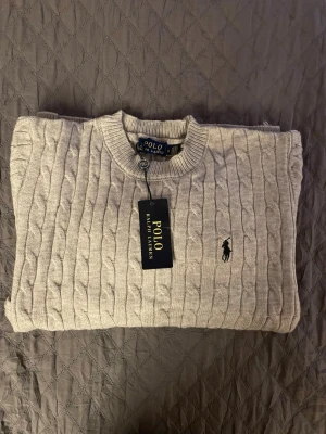 Ljusgrå  tröja Polo Ralph Lauren - Säljer en gråstickad tröja från Polo Ralph Lauren. Helt ny och aldrig använd. Storlek S. Klassisk och tidlös design som passar till allt.  Skickas snabbt 📦 Skriv vid frågor!