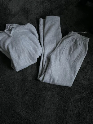Grå mjukisset  - Säljer ett par grå mjukisbyxor med elastisk midja och snörning. Byxorna har en bakficka och är gjorda i mjukt bomullsmaterial, perfekta för chill dagar hemma eller när du vill vara extra bekväm. Enkel och stilren design som passar till hoodie eller t-shirt. (Går även köpa separat)