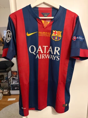 Barça Messi 10 matchtröja 2015 - Säljer en ikonisk FC Barcelona matchtröja från Champions League-finalen 2015 med Messi 10 på ryggen. Tröjan har breda marinblå och röda ränder, gula detaljer och officiella tryck. Tillverk sopolyester med Dri-FIT-teknik för bästa komfort.