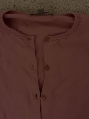 Rosa kofta från Uniqlo, storlek S - Säljer en mjuk och tunn rosa kofta från Uniqlo i storlek S. Koftan har rund hals, långa ärmar och knappar framtill. Materialet är bomull och passformen är normal. Perfekt att slänga på sig när det är lite kyligt ute.