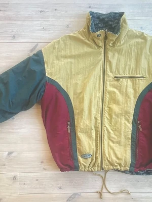 90s Craft Snowboardjacka – Vintage / Retro - Riktigt snygg och välbevarad snowboardjacka från 1990-talet, tillverkad av Craft. Jackan är i nyskick och har den där äkta retrolooken med färgblock i beige, grönt och vinrött – precis som snowboardmodet såg ut på 90-talet.  x Snölås i midjan – perfekt för puderåkning x Två innerfickor med blixtlås x Tre ytterfickor med blixtlås x Varm och skön stickad insida x Dragsko i midjan för justerbar passform Ett grymt fynd för dig som älskar vintage, snowboardretro eller bara vill ha en unik jacka.