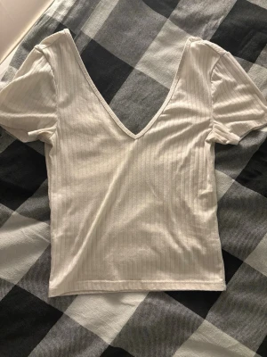 Vit ribbad topp med v-ringning - Säljer en vit ribbad topp med djup v-ringning fram och baktill med korta ärmar. Toppen har en smickrande slim passform, Perfekt för dig som gillar enkla och stilrena plagg.