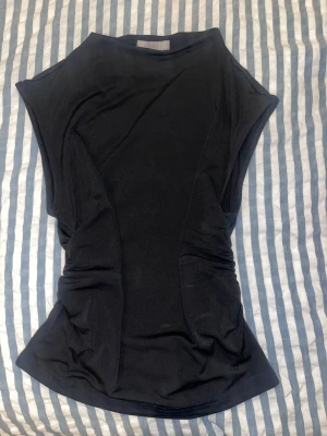 Svart topp från H&M med rynkade sidor - Svart figursydd topp från H&M i storlek S. Toppen har rynkade detaljer på sidorna och är ärmlös. Aldrig använd. Pris går att diskutera💕