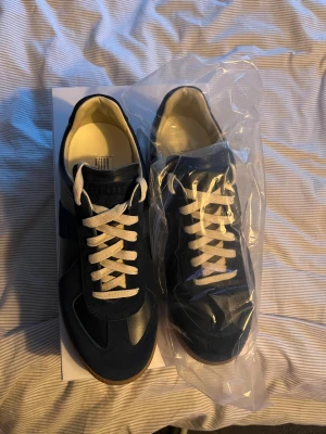 Maison Margiela gats - Maison Margiela sneakers i navy blue med kontrasterande vita snören och beige insida. Klassisk rund tå och platt sula. Snygg retrostil med stilrena paneler och detaljer. Kommer i originalkartong. Perfekt för dig som gillar exklusiva och tidlösa sneakers. 