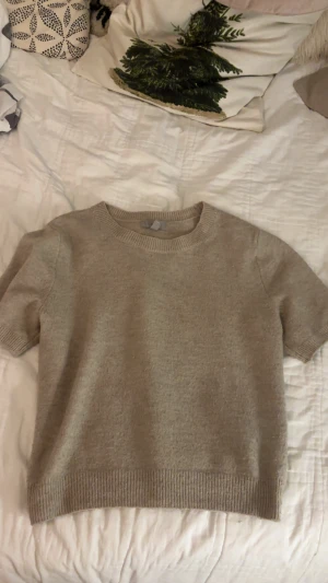 Beige stickad kortärmad tröja från hm! - Snygg beige stickad tröja med korta ärmar och rund hals. Tröjan har ribbade muddar vid ärmslut och nederkant, vilket ger en clean och stilren look. Perfekt för lager-på-lager under hösten eller våren.