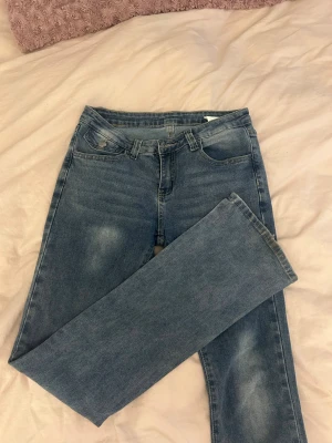 Blå bootcut jeans med fickdetaljer - Snygga blå jeans med utsvängda ben och klassisk femficksdesign. Baktill finns fickor med lock och knapp, vilket ger en cool touch. Jeansen har bälteshällor och är tillverkade i ett mjukt denimtyg som är skönt att ha på sig. Perfekt för dig som gillar enkel och stilren look.