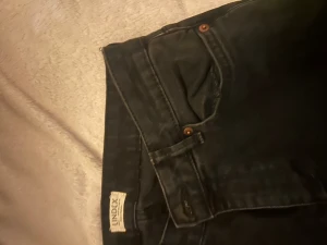 Svarta bootcut jeans från Lindex - Säljer ett par svarta jeans från Lindex i klassisk bootcut-modell. Jeansen har hög midja och är tillverkade i ett stretchigt bomullsmaterial som sitter snyggt och bekvämt. Perfekt passform och stilren look med knapp och dragkedja framtill.
