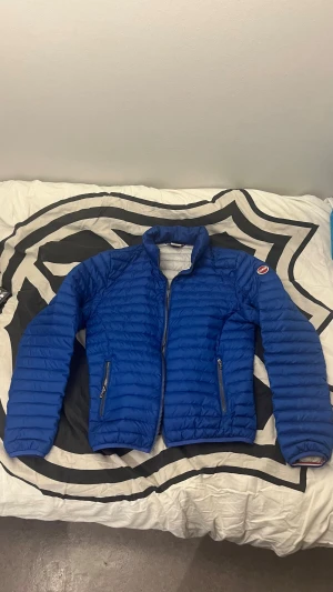 Blå Colmar pufferjacka  - Blå pufferjacka från Colmar med snyggt quiltad design och dragkedjor på fickorna. Jackan har hög krage och Colmar-logga på ärmen. Perfekt för dig som vill ha en lätt och stilren jacka med sportig vibe saknar löpare.