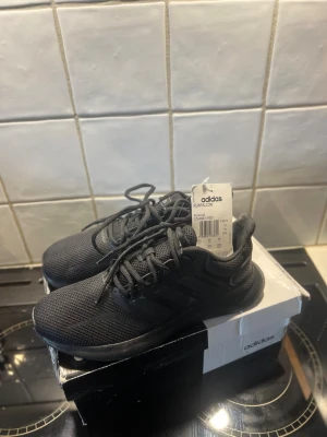 Svarta Adidas Runfalcon sneakers - Säljer ett par svarta Adidas Runfalcon sneakers med mesh-överdel och klassiska tre ränder på sidan. Skorna har snörning och platt sula, perfekt för dig som gillar sportig stil. Materialet är syntet och mesh för bra ventilation och komfort.