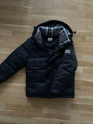 Burberry jacka & väst - En mångsidig och mycket populär Burberry-jacka som kan bäras både som jacka och väst. Den är använd en vinter men är fortfarande i mycket gott skick. Inga defekter. Storlek M men passar mer som S.(Modellen är 171cm/65kg). längd:66cm