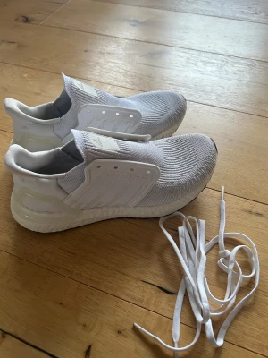 Adidas Ultraboost vita sneakers - Säljer ett par vita Adidas Ultraboost sneakers med stickad ovandel i syntetmaterial och platt sula. Skorna har en rund tå och kommer med vita skosnören vid sidan. Perfekta för träning eller chill vardagsstil.