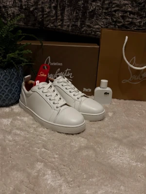Vita sneakers från Christian Louboutin - Säljer ett par stilrena vita sneakers från Christian Louboutin i skinn. Skorna har klassisk rund tå, snörning och den ikoniska röda sulan med logga. Perfekta för dig som vill ha en clean look med exklusiv känsla.