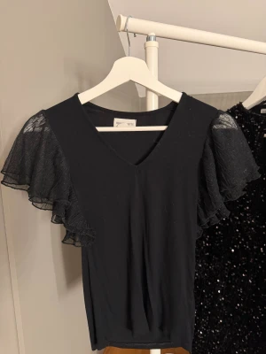 Svart blus med volangärmar Holly & Whyte - Supersnygg svart blus från Holly & Whyte i storlek xs med v-ringning, tröjan har inte används många gånger men har inga skador och kommer inte längre till användning🤍