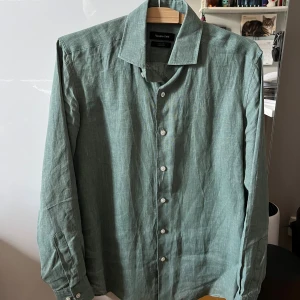Grön linneskjorta från Massimo Dutti - Snygg grön skjorta i 100% linne från Massimo Dutti. Skjortan har klassisk krage, vita knappar framtill och långa ärmar med manschett. Perfekt för en chill och stilren look under varmare dagar. Knappast använd, passar även M.