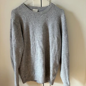 Grå stickad tröja från John Henric - En klassisk grå stickad tröja från John Henric. Tröjan har rund halsringning, ribbade muddar och är långärmad. Perfekt för lager-på-lager under hösten och vintern. Enkel och stilren design som funkar till allt.