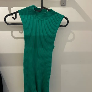 Grön ribbad polotopp - Superfin grön ribbad polotopp utan ärmar – stilren och lätt att matcha! Sitter tajt och framhäver figuren. Passar lika bra till jeans som till kjol. I toppskick.