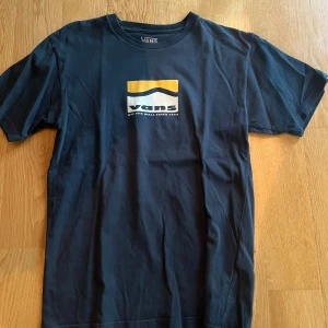 Mörkblå Vans t-shirt med tryck - Snygg mörkblå t-shirt från Vans med klassiskt logotryck i vitt och gult på bröstet. T-shirten sitter ganska tajt så pasaar även XS.. 