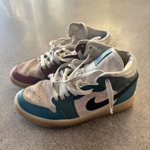 Air Jordan 1 Mid Anti-Gravity Machines sneakers - Säljer ett par Nike Jordan 1 i gott skick med unik färgblockning i rött, blått, vitt och beige. Skorna har svart swoosh, högt skaft och klassisk snörning. Ovandelen är i skinn och textil, med gummisula och perforerad tå för extra stilpoäng. Storlek EUR 38. Nypris 2 682 kr. 